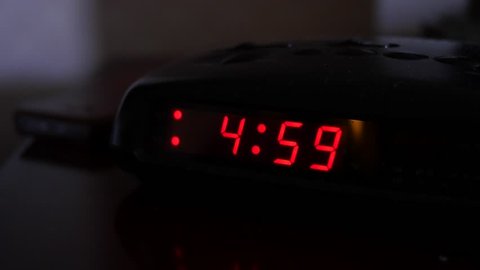 A man turns off the alarm when a digital alarm clock turns to five o'clock