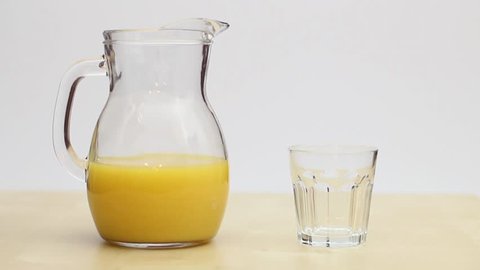 a hand takes the juice jar and pours a glass with orange juice