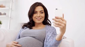 pregnancy, motherhood, technology, people and expectation concept - happy pregnant woman with smartphone using video chat and waving hand at home