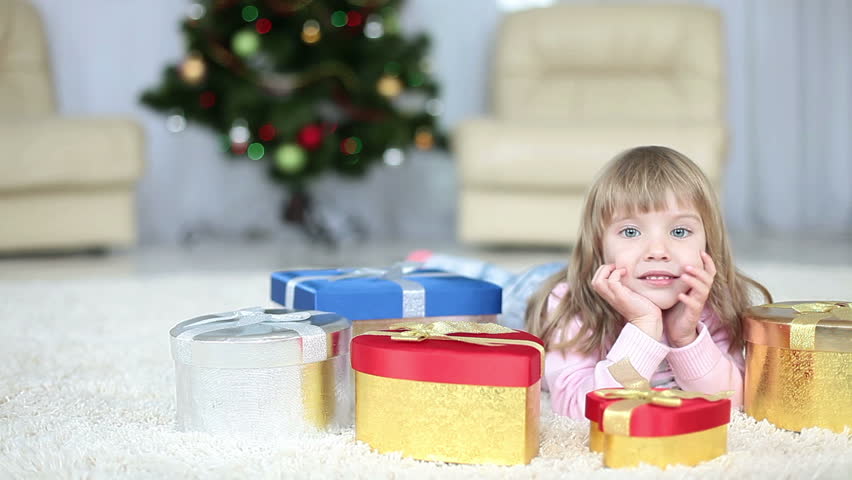 Girl with christmas  gifts lying on the carpet. Looking at camera 