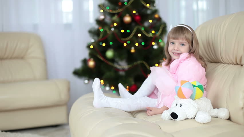 Happy little girl sitting on a sofa near the Christmas tree. 