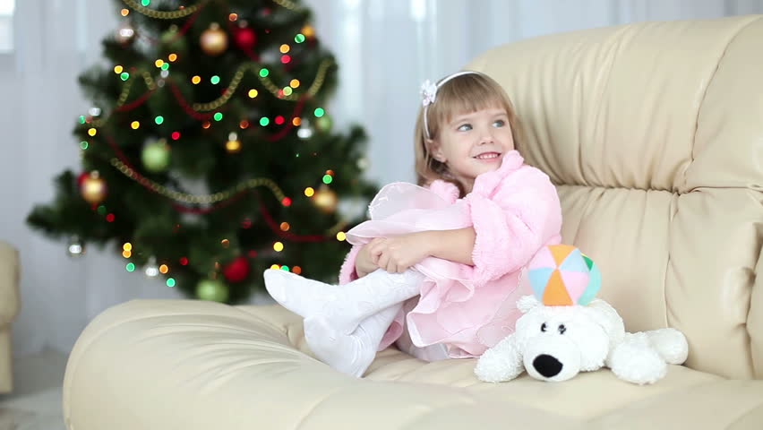 Happy little girl sitting on a couch near the Christmas tree. 