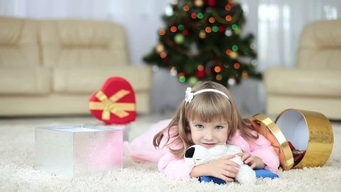 Happy little girl with gifts lying on the carpet near the Christmas tree. 