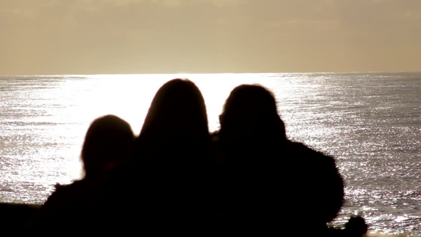 Silhouette of family taking pictures in front of the sunset over the ocean