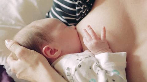 Newborn baby girl during breastfeeding, helping herself with her hand