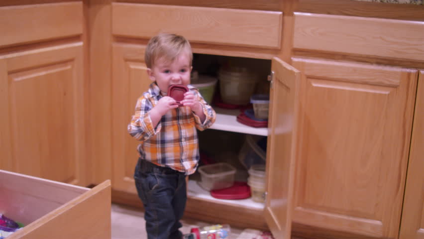 Little boy playing with plasticware in the kitchen and putting it in his mouth