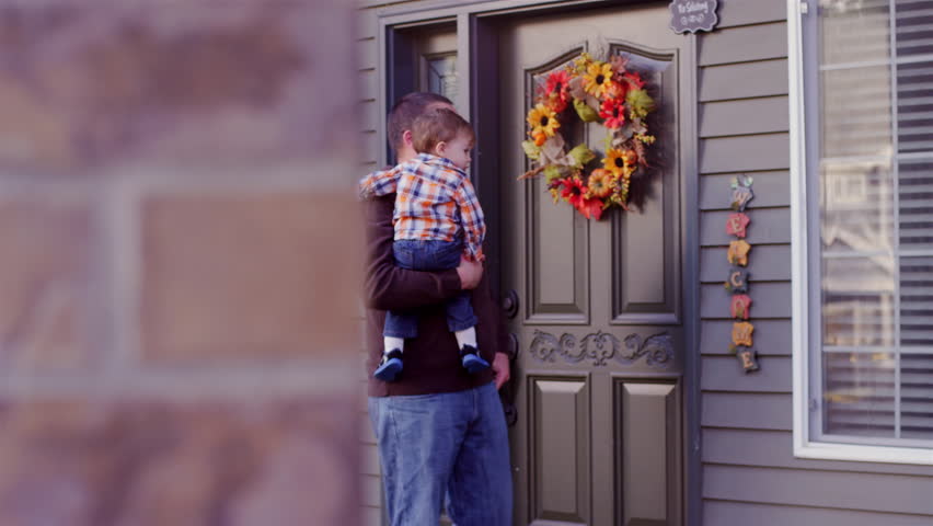 A father holding his baby boy and walking in front of their house
