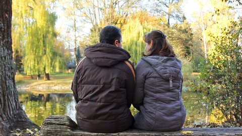 couple sits on bench in beautiful autumn park near lake, then he hugs her