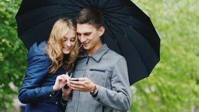 Young couple enjoys a smartphone - standing under an umbrella, the rain. Connected in any weather