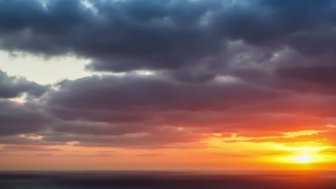 4k timelapse clouds crossing the amazing sky over the sea or ocean at sunset. Sun rays emerge through the clouds. The clouds cross slowly from right to left and appear to be orange blue and purple. 