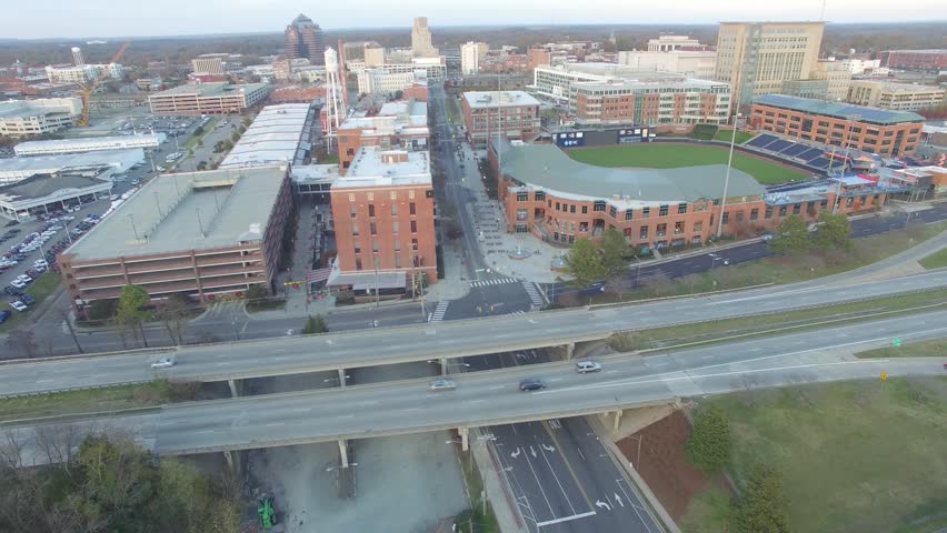 Aerial shot showing the American Tobacco Campus and the Durham Bulls Athletic Park in downtown Durham, North Carolina, as well as a few cars driving down NC-147.