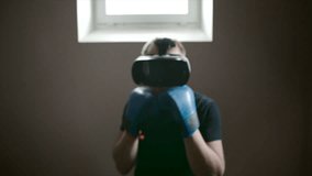 Young man is boxing with virtual rival in the gym using VR glasses