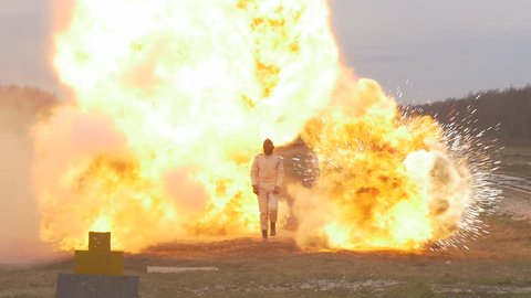 Stunt girl in a fiery explosion. Slow motion. Beautiful girl stunt runs across the field through the explosions and fire.