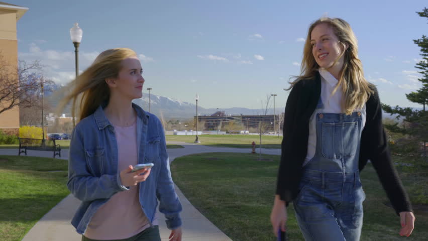Friends Talk On A Walk Around Campus, They Check Their Smart Phones, Then Find A Bench To Sit Down 