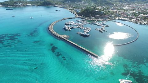 Flying over crystal blue sea waters, revealing boats and yachts. Aerial view of the marina in St. Martin. The Caribbean island of French Saint Martin. Sunrise light bouncing off the Caribbean sea. 