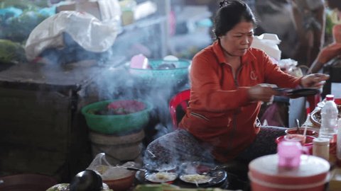 Outside Nha Trang, Vietnam - May 8 2015: Local life of ordinary people in poor traditional city of Indochina. Woman prepares food, noodles for customers. Work and business in roadside bazaar. Outdoors