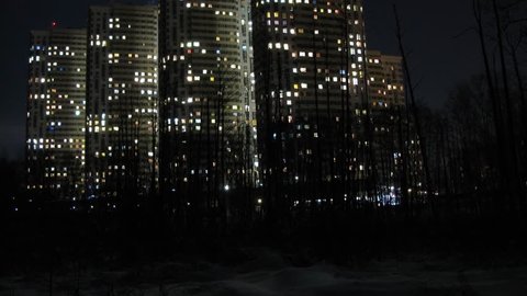 The moon appears from behind the buildings at night. Time lapse.
