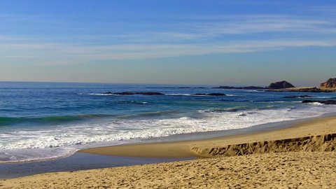 Shot of the Pacific Ocean and rocky coastal Aliso Beach in the city of Laguna Beach, California. This clip features a plain view of the ocean waves and sandy beach without people in the shot.
