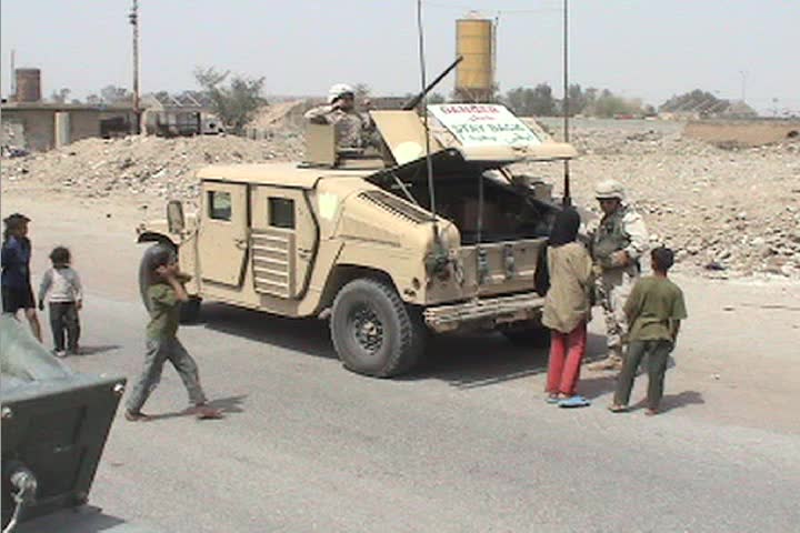 A Marine unloads bottled water and other goods from a transport and hands it to villagers in Iraq.