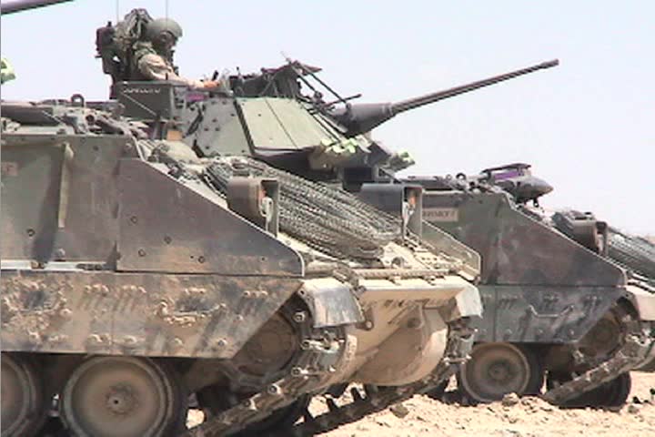 A line of American army tanks sits awaiting combat operations in the Iraqi desert.