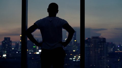 Young man admire view from window at home at night
