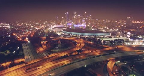 Aerial view of city traffic on freeway interchange at night flying forward to downtown Los Angeles skyline in background. 4K UHD.