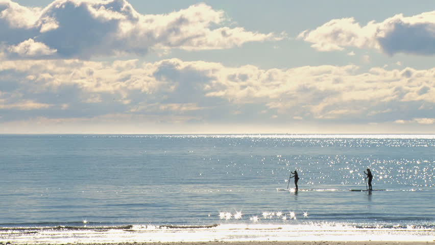 A man and woman paddle their boards languidly on sparkling bay waters.