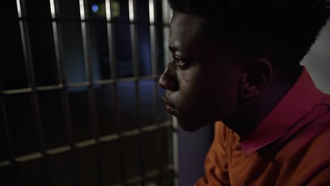 Young man looking out from his prison cell through the bars of jail