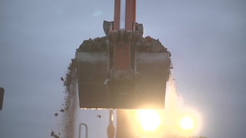 Bulldozer charging shovel with sand and transporting to pile, close up, excavator creating heap at  construction site. Separating ground. Slow motion shot in the dusk.