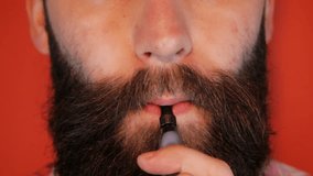 Man with a beard smoking an e-cigarette (electronic cigarette), on a red background. Slow-motion video. Full hd video clip 1080p.