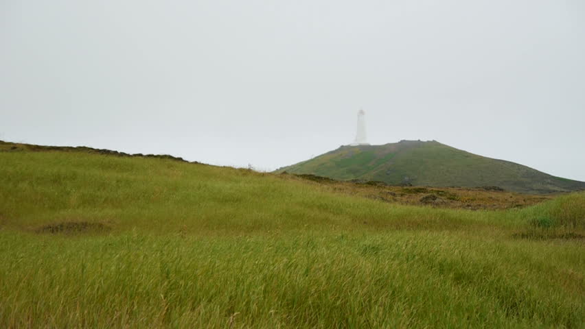 Lighthouse on a grassy hill. Misty and windy weather. Iceland.