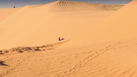 tourist tries draw out quad from sand at foot of sand dune against sand background