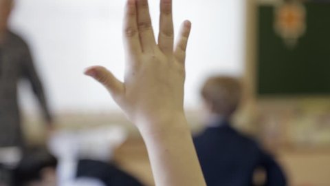 A group of primary school children raise their hands to answer the teacher’s question. Close up on the hand of a girl. Handheld tracking shot.