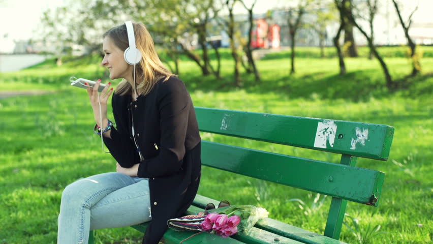 Happy girl sitting in the park and talking on cellphone 
