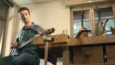 Man at work as craftsman in italian workshop playing and testing new bass guitar and musical instrument, artisan atelier, art