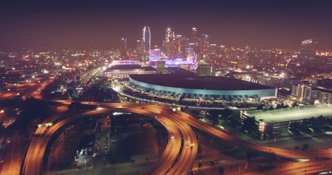 Aerial view of city traffic on freeway interchange at night flying backwards with downtown Los Angeles skyline in background. 4K UHD.