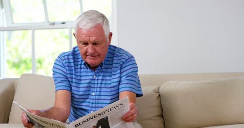 Mature Caucasian man reading newspapers on sofa at home 