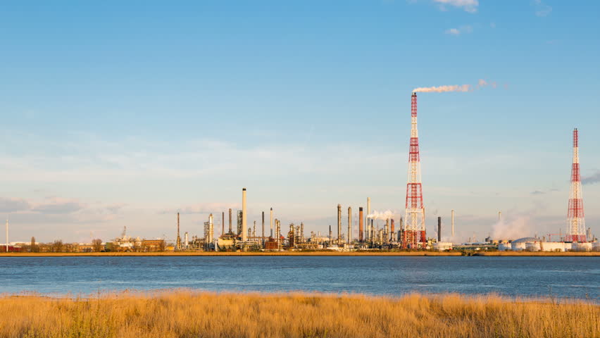 Panning timelapse sequence of a large oil refinery in the harbor of Antwerp, Belgium with blue sky and warm evening light.