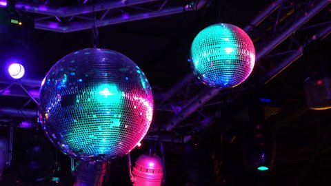 Spinning disco ball in night club 4k Decorative mirrored balls spin and reflect colorful teal and pink light around concert stage area in dark club.