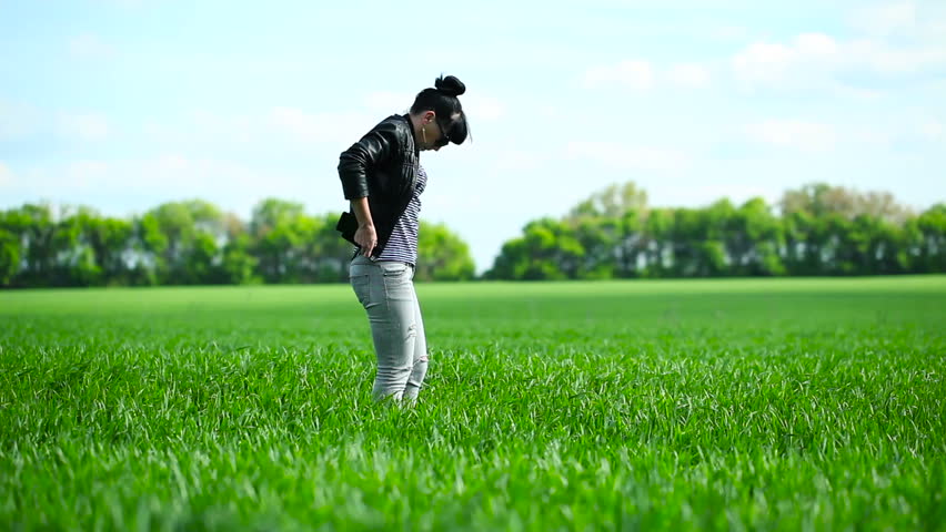The girl goes on a field of green wheat growing. White clouds over the field. Spring Season