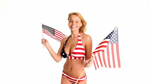 Sexy young blonde woman in red, white and blue bikini waving two American Flags.