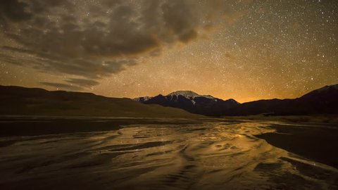 Spring Night at Great Sand Dunes National Park & Preserve - Time-lapse of spinning starry night sky over spring Medano Creek,  snow-capped peaks, and sand dunes in Great Sand Dunes National Park.