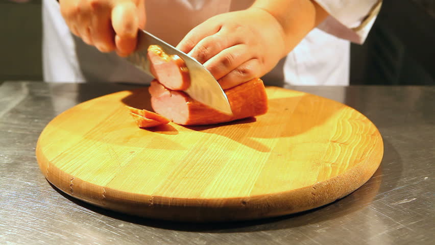 Chef cuts on a cutting board large piece of ham