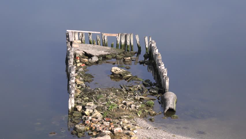 Remains of wooden structure on banks of river, smooth water surface, Central Europe
