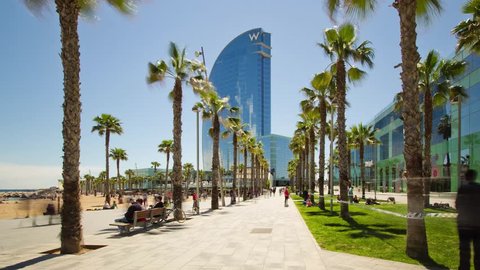 Barcelona, Spain - May 1, 2016: 4K Hyperlase (timelapse) approaching the facade of the W Barcelona (Hotel Vela) through palm trees, located in the Barceloneta district, next to the beach.