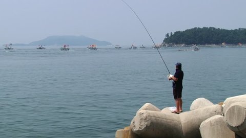 TONGYEONG, KOREA - AUGUST 17, 2013: Unidentified man does fishing with boats departing from harbor during Hansan festival at the background in Tongyeong, Korea.

