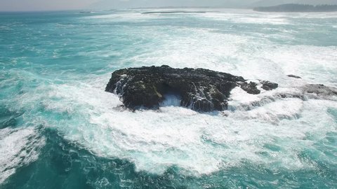 Aerial shot of ocean waves and cliff - waves washing up on a rock in sea