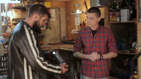 Guy talking about of motorcycle with car mechanic in garage