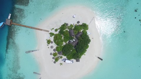 Aerial shot of a small tropical island in Maldives island, 2015.
Palms and jetty on the sandbank. Camera rise up.