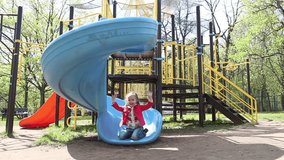 Adorable little girl has fun riding on a slide at playground in the park at the day time
